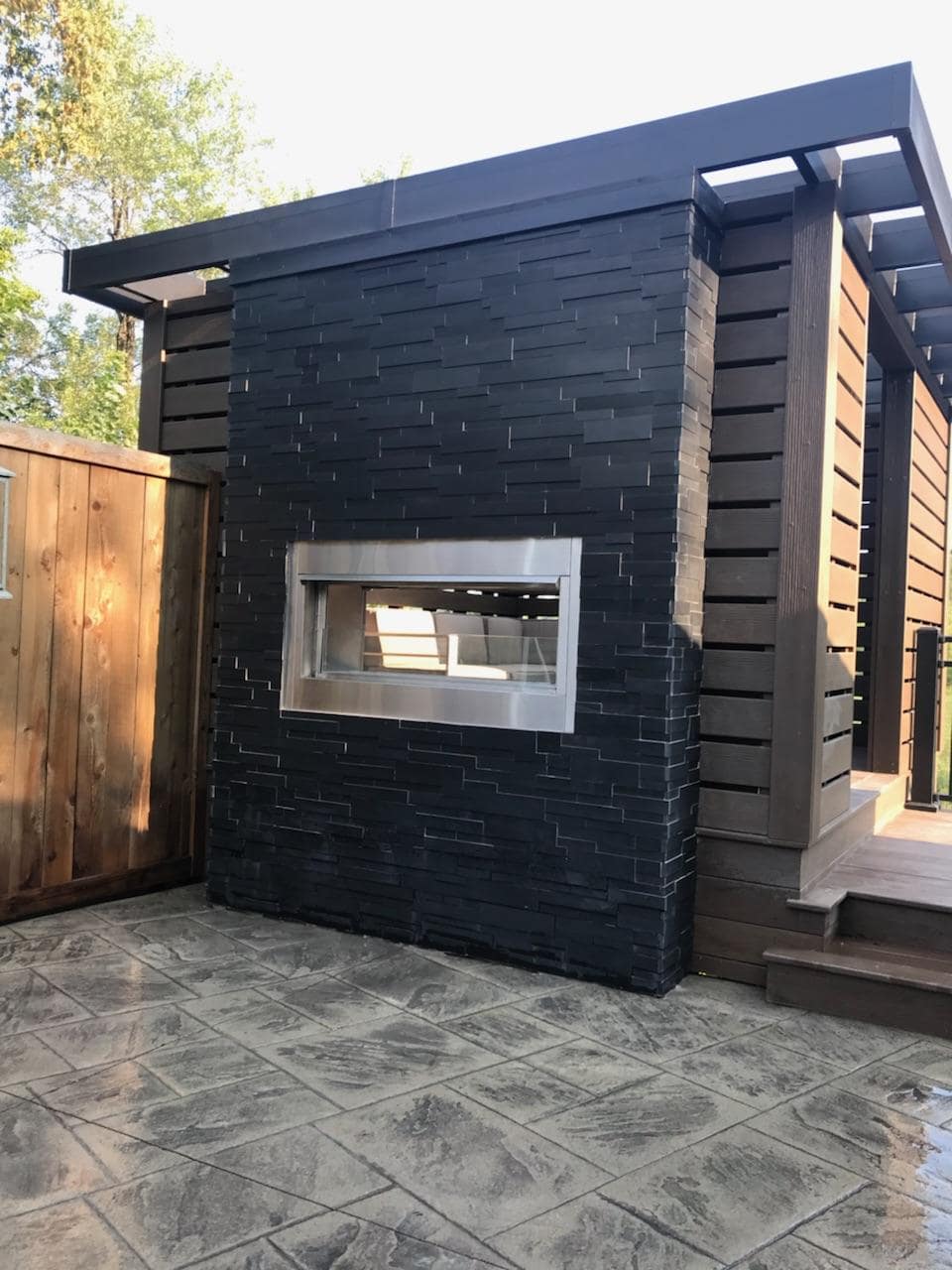 View from open air patio of a two sided fireplace clad with Norstone's Ebony Aksent 3D Stone Panels.
